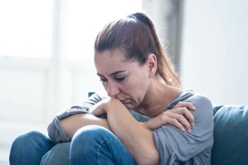 pensive woman scrunched up on couch wondering what is ghb gamma hydroxybutyrate