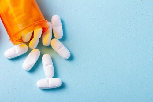 orange prescription bottle spills white pills on blue background showing what is oxycontin