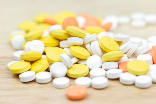 large pile of yellow white and orange pills show what is vicodin