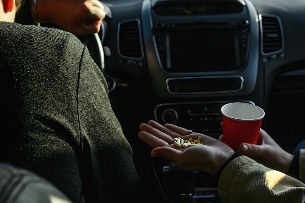 Two people sitting in a car with pills in hand