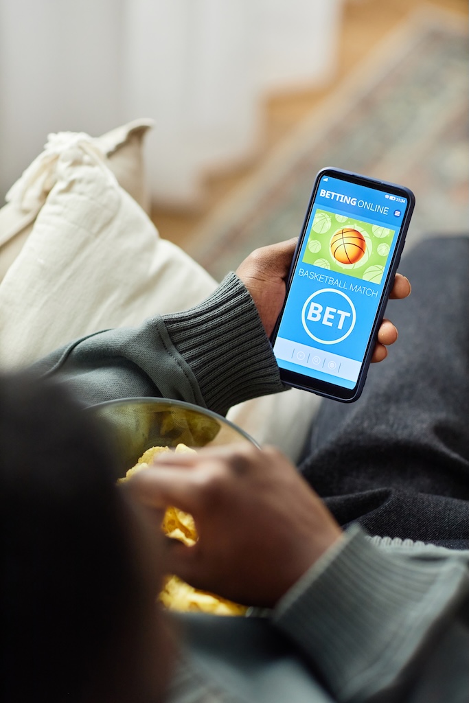 Top view shot of man holding phone with gambling app on screen and eating at home