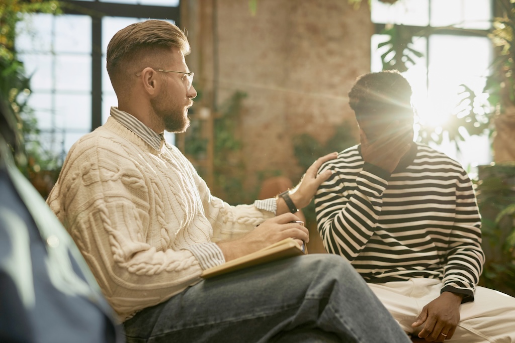 Side view portrait of bearded male psychologist supporting client during therapy session