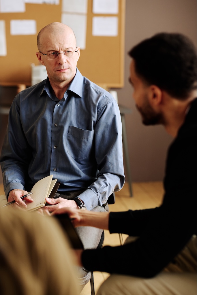 Confident mature counselor looking at one of patients struggling with marijuana addiction in therapy session