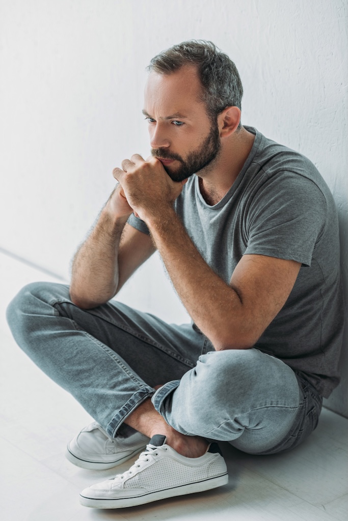 high angle view of sad bearded man sitting in floor and looking away