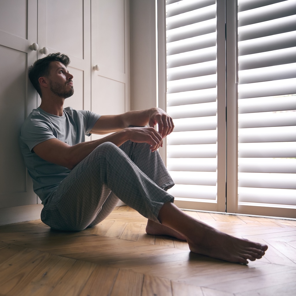 Depressed Man Suffering With Poor Mental Health Sitting On Floor At Home
