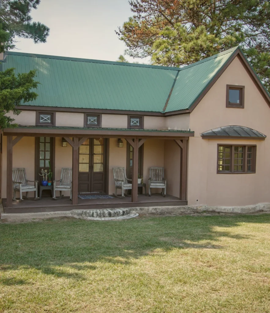 A stucco bunkhouse with a green metal roof and a covered porch lined with rocking chairs at The Last Resort ranch.