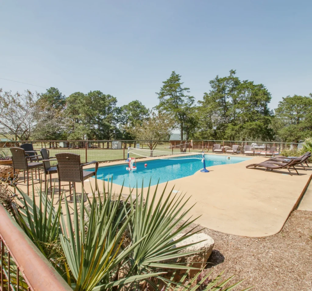 The fenced outdoor swimming pool with patio furniture and lounge chairs at The Last Resort ranch.