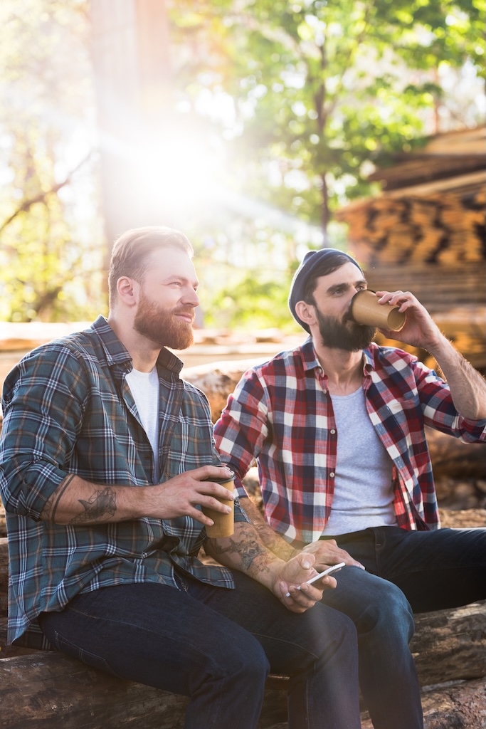 Two men sitting in outdoor group therapy session drinking coffee