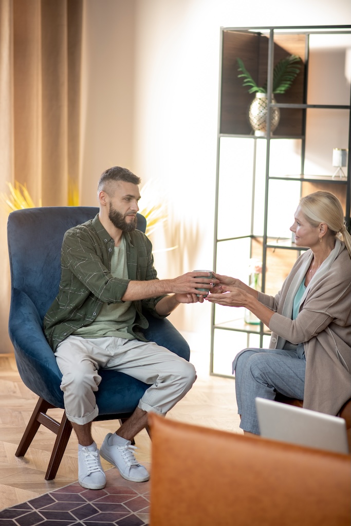 Pleasant psychoanalyst giving cup of tea to her patient having long talk